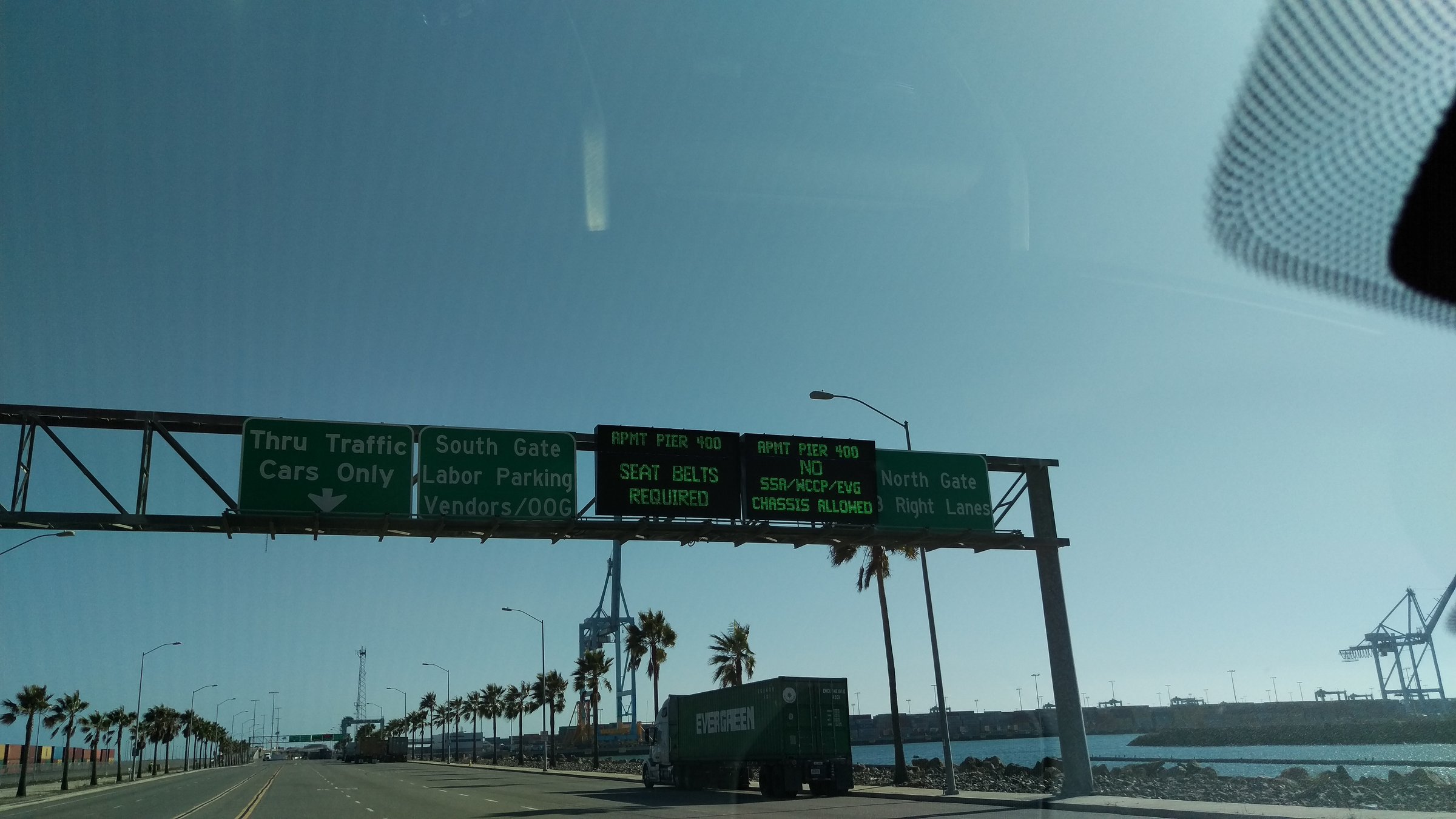 Overhead LED message boards at the Port of Los Angeles directing traffic to APM Terminals Pier 400 with seat belt and chassis restrictions